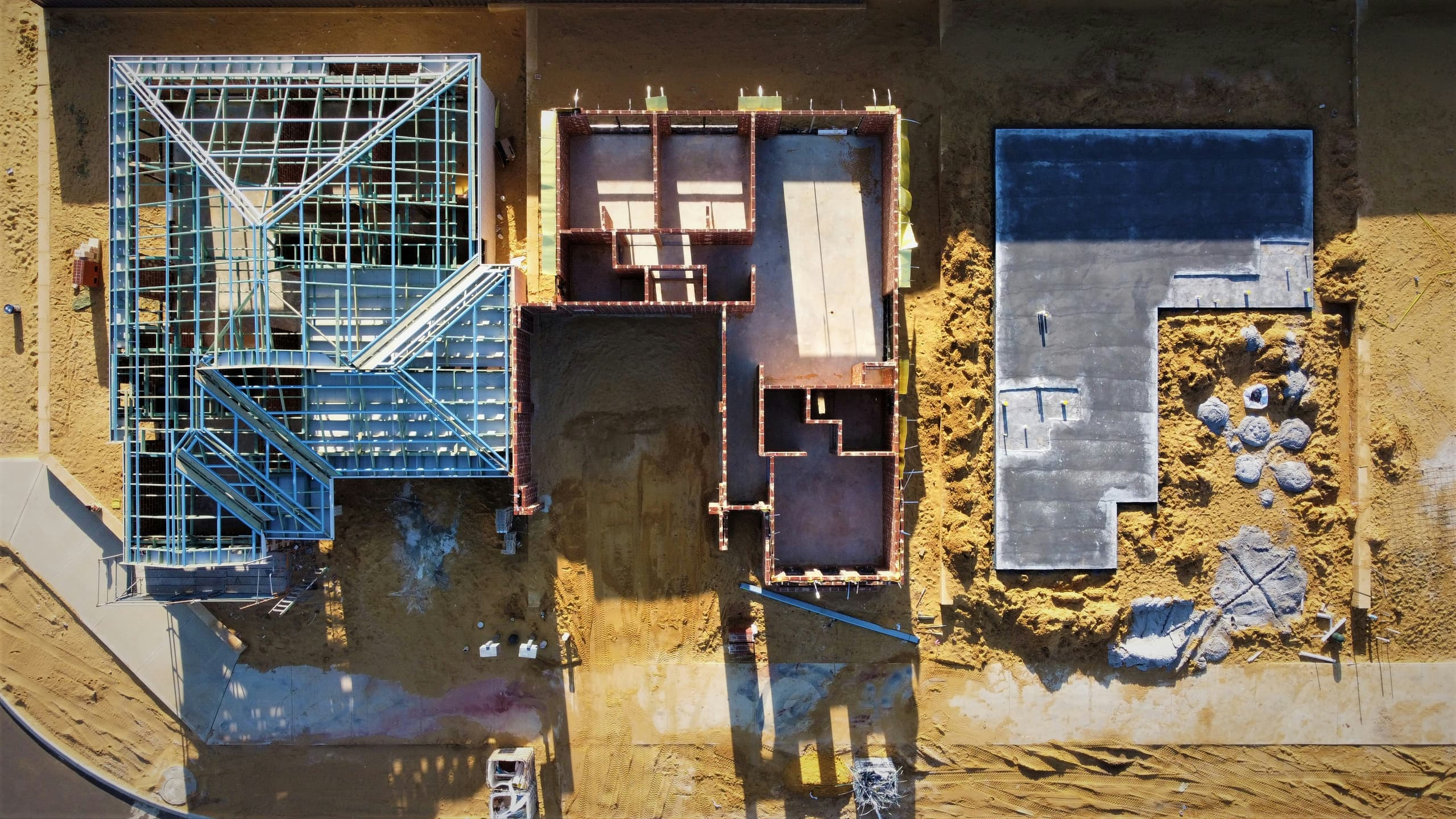 An overhead view of a residential construction site mid-frame — foundations, steel framing, and flat roofs under the Colorado sun